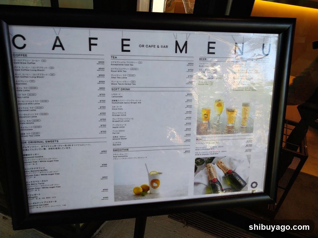 A framed menu board displaying coffee, tea, beer, soft drinks, sweets, and smoothies with prices in yen.