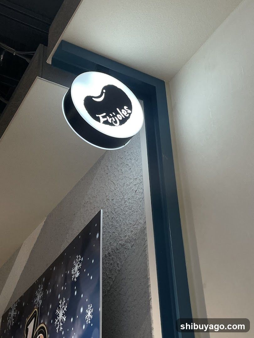 A circular illuminated sign with a black silhouette of an apple and the word 'Ejybles' in white script is mounted on a dark blue frame attached to a light-colored wall. Below, part of a poster featuring snowflakes and a number '70' is visible.
