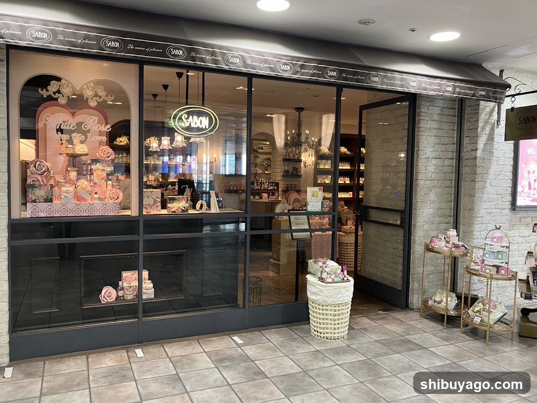 A shop front with large glass windows displaying pink-themed products and a 'White Love' sign inside. The exterior features a brick wall, tiled floor, and hanging baskets of merchandise outside the entrance.