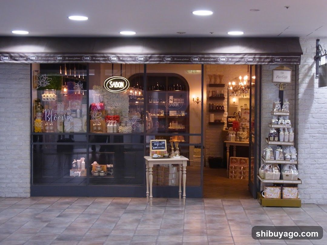 The image shows the exterior of a shop named 'SABON', featuring large glass windows and doors with warm interior lighting visible through them. A small table stands in front displaying products, while shelves to the right hold gift items.