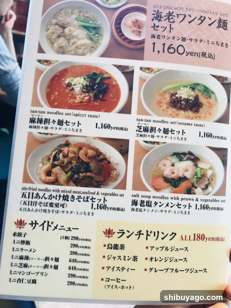 A printed menu featuring shrimp won ton noodle sets, spicy and sesame flavored noodles, stir-fried soba with mixed ingredients, salt soup noodles with prawn, side dishes like udon and mini ramen, and lunch drinks including tea and juices.
