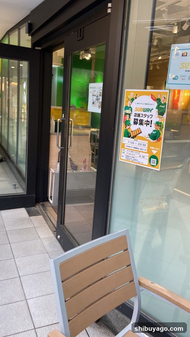 Exterior view of a Subway restaurant entrance featuring glass doors and windows with a recruitment poster on the right side displaying staff information and contact details.