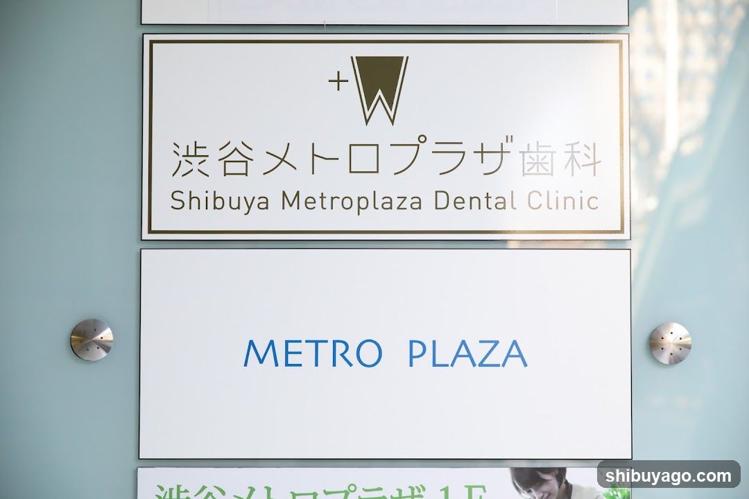 The image shows the exterior signage of a dental clinic located at Shibuya Metroplaza. The top sign displays the name 'Shibuya Metroplaza Dental Clinic' in both Japanese and English, along with a logo featuring a stylized tooth shape. Below it is another sign reading 'METRO PLAZA' in blue text. Two metallic circular fixtures are visible on either side of the lower sign.