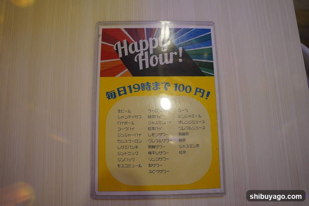 A printed Happy Hour menu board displaying daily specials at 100 yen until 7 PM, featuring a list of beverages and drinks.