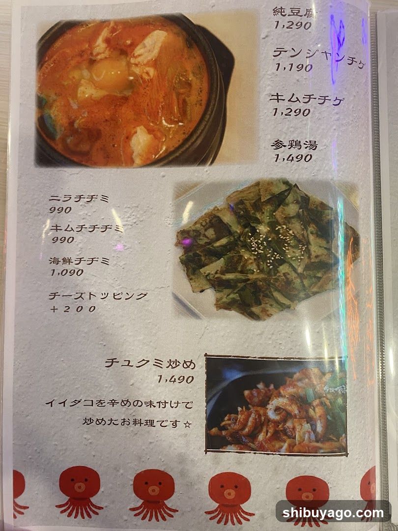 A printed menu page featuring photos of dishes alongside Japanese text descriptions and prices in yen. Items include soup, kimchi, fried pancakes, and stir-fried seafood.