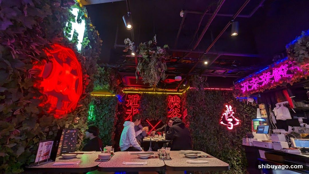 Interior of a neon-lit restaurant with greenery walls and customers dining
