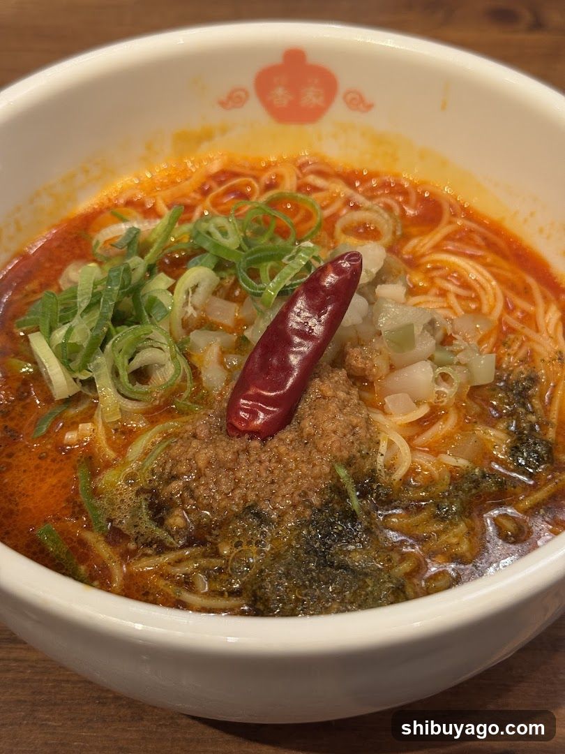 A close-up of a bowl of spicy ramen with red broth, green onions, minced meat, and a dried chili pepper on top.