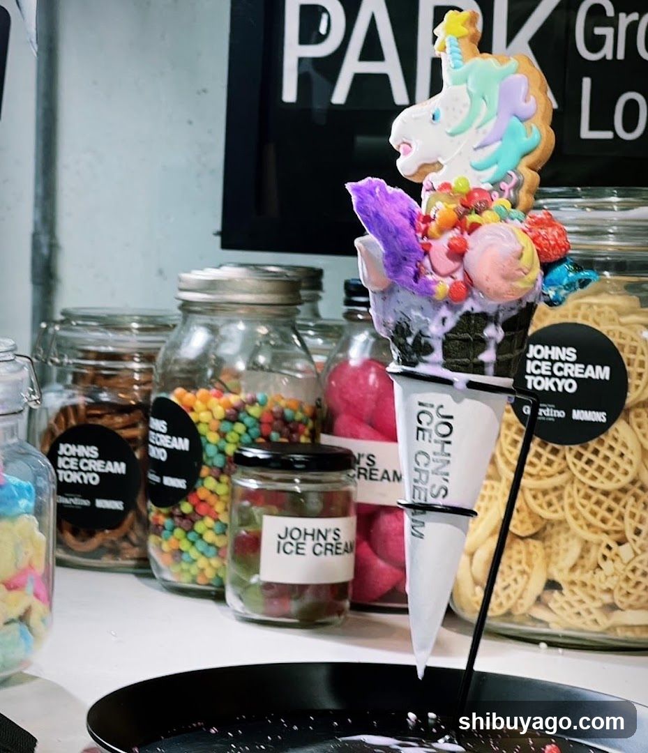 A colorful ice cream cone with unicorn-themed toppings sits in the foreground, surrounded by glass jars filled with assorted candies and snacks. The background features a sign reading 'PARK' and partial text suggesting a shop environment.