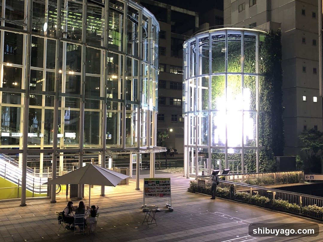 Night scene with glass structures and people sitting under an umbrella
