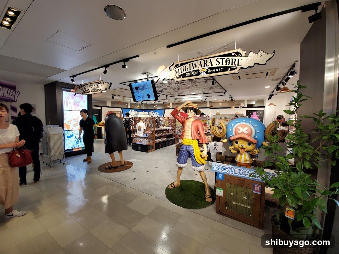 Interior view of a One Piece themed store featuring large statues of Monkey D. Luffy and Chopper, branded signage reading 'MUGIWARA STORE', shelves stocked with merchandise, customers browsing, and decorative plants.