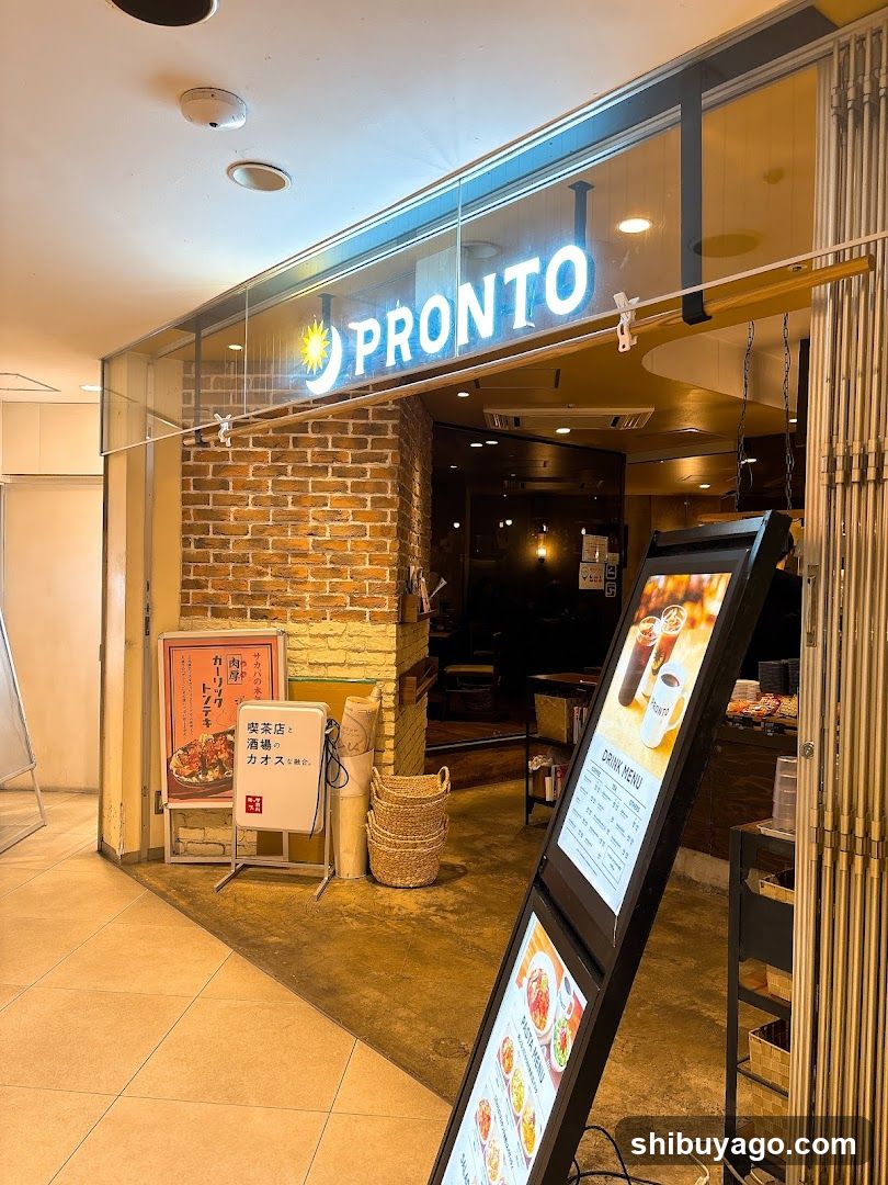 A shop with a glass facade and brick wall, featuring illuminated signage reading 'PRONTO' above the entrance. A digital menu board stands outside displaying food items and prices. Inside, warm lighting illuminates the interior space.
