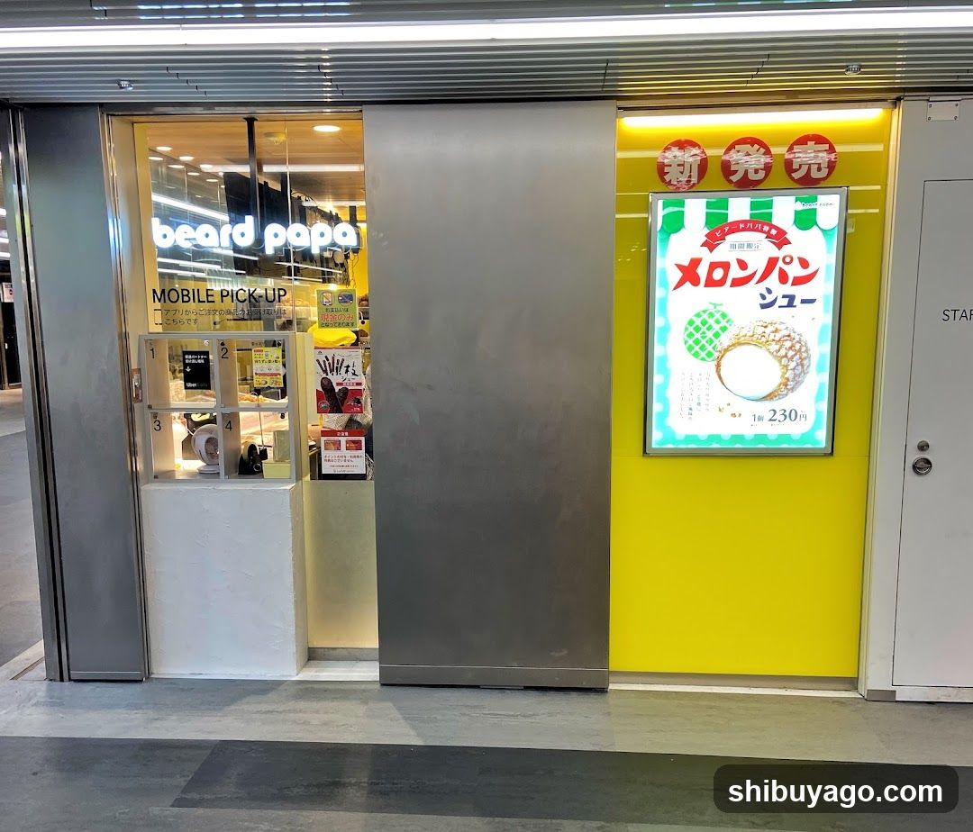 The image shows the exterior of a shop called 'beard papa' with visible signage on the building facade. A bright yellow wall features an illuminated poster advertising 'melon pan shoes' priced at ¥230. The entrance includes glass doors and windows displaying interior items, including numbered shelves and promotional materials inside.