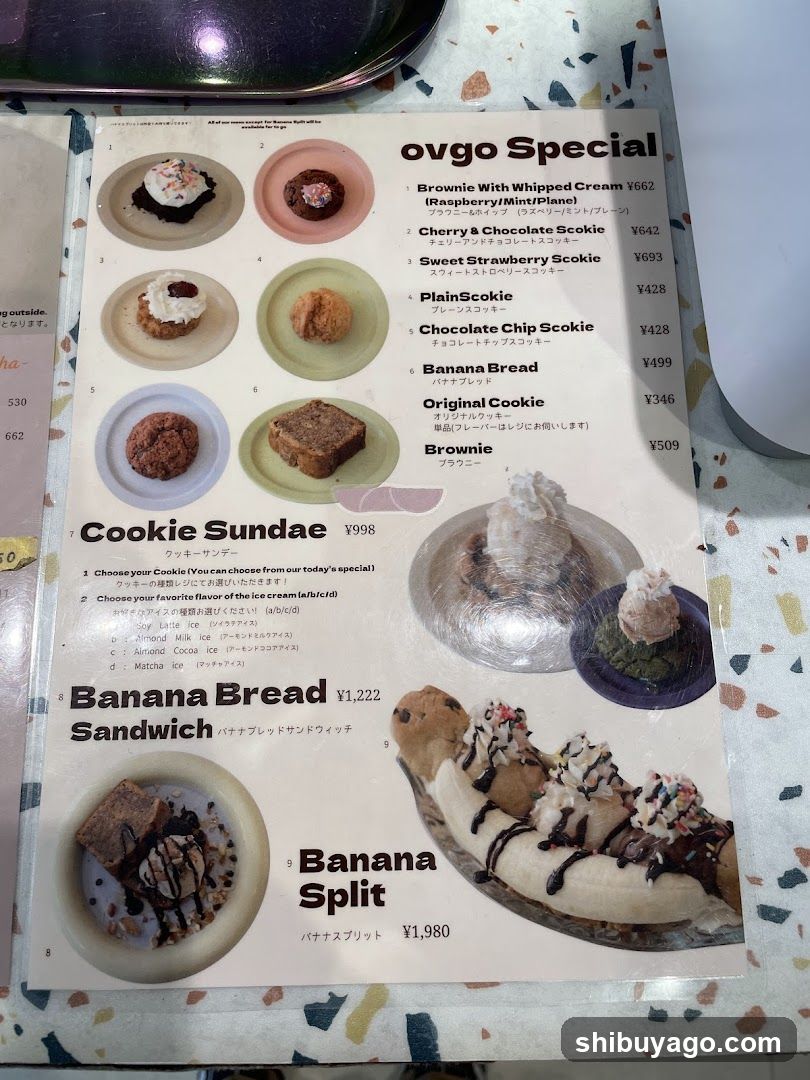 A printed menu page featuring dessert items with prices in Yen, including Brownie With Whipped Cream, Cherry & Chocolate Sookie, Sweet Strawberry Sookie, Plain Sookie, Chocolate Chip Sookie, Banana Bread, Original Cookie, and Brownie under the 'ovgo Special' section. Below that is a 'Cookie Sundae' option with customizable cookie types and ice cream flavors like Joy Little Ice, Minty Ice, Aralad Cocoa Ice, and Matcha Ice. Further down are Banana Bread Sandwich priced at ¥1,222 and Banana Split at ¥1,980, each accompanied by corresponding photos of the desserts.