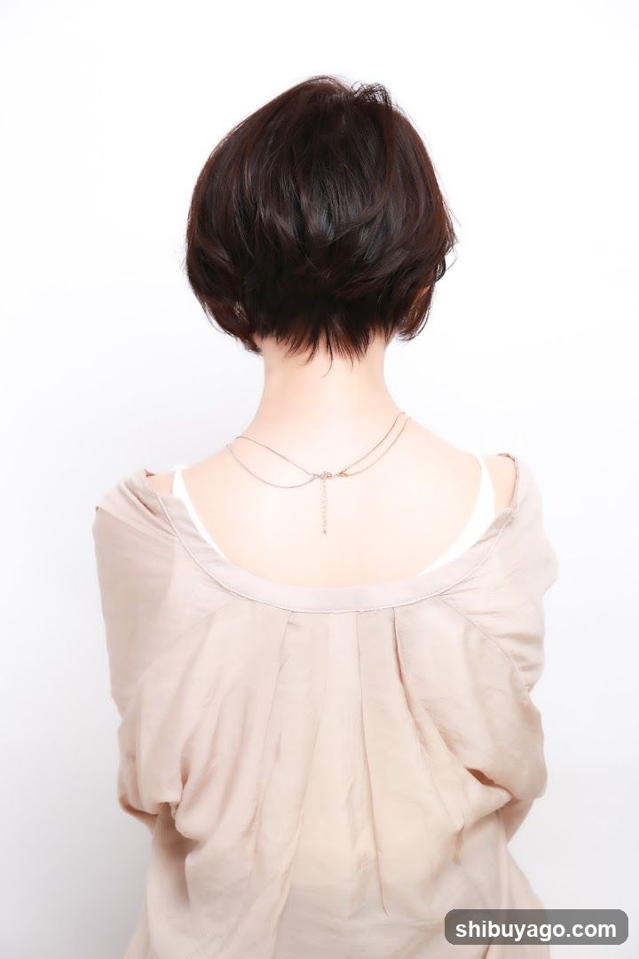 Back view of a person with short dark hair wearing a beige top and necklace