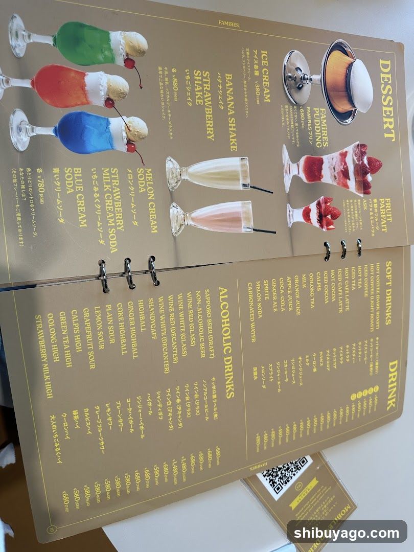 A spiral-bound menu displaying desserts, soft drinks, alcoholic beverages, and juices with prices in yen.