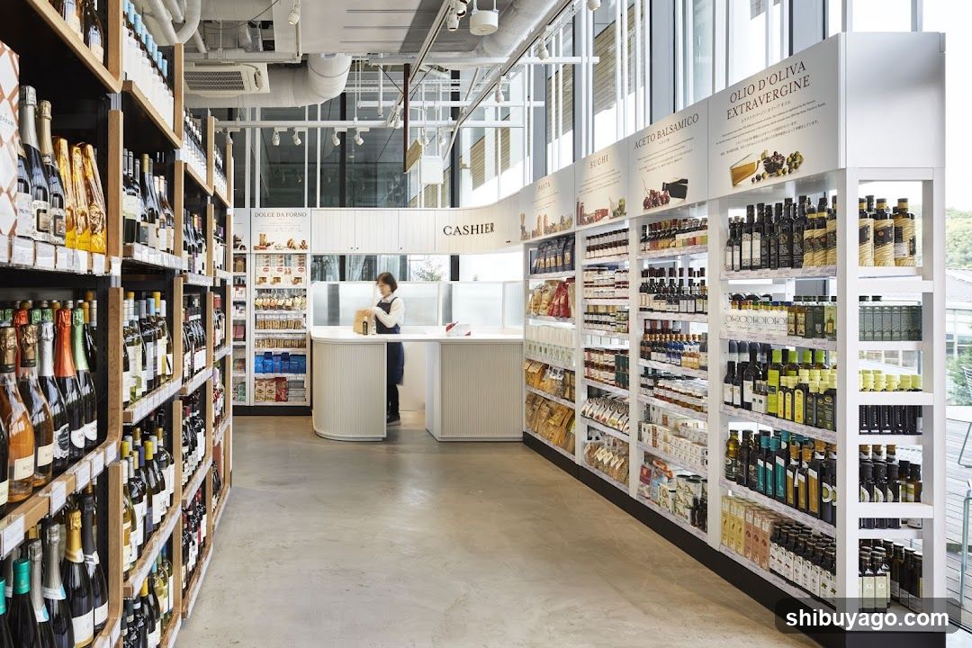 Interior of a well-lit grocery store with extensive wine and olive oil sections, featuring a cashier counter in the background.