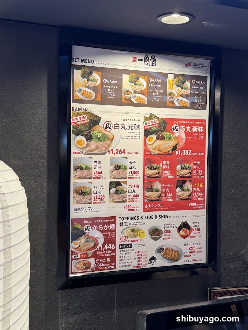 A framed menu board displaying various ramen set menus, including 'Shiro-maru' and 'Akamaru', with prices in yen. The menu also lists toppings and side dishes like 'Kara-u' and 'Gyoza'.