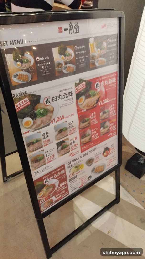 A framed menu board displaying various ramen dishes with prices in Japanese yen, featuring items like '白丸元味' and '赤丸新味', along with toppings and side dishes.