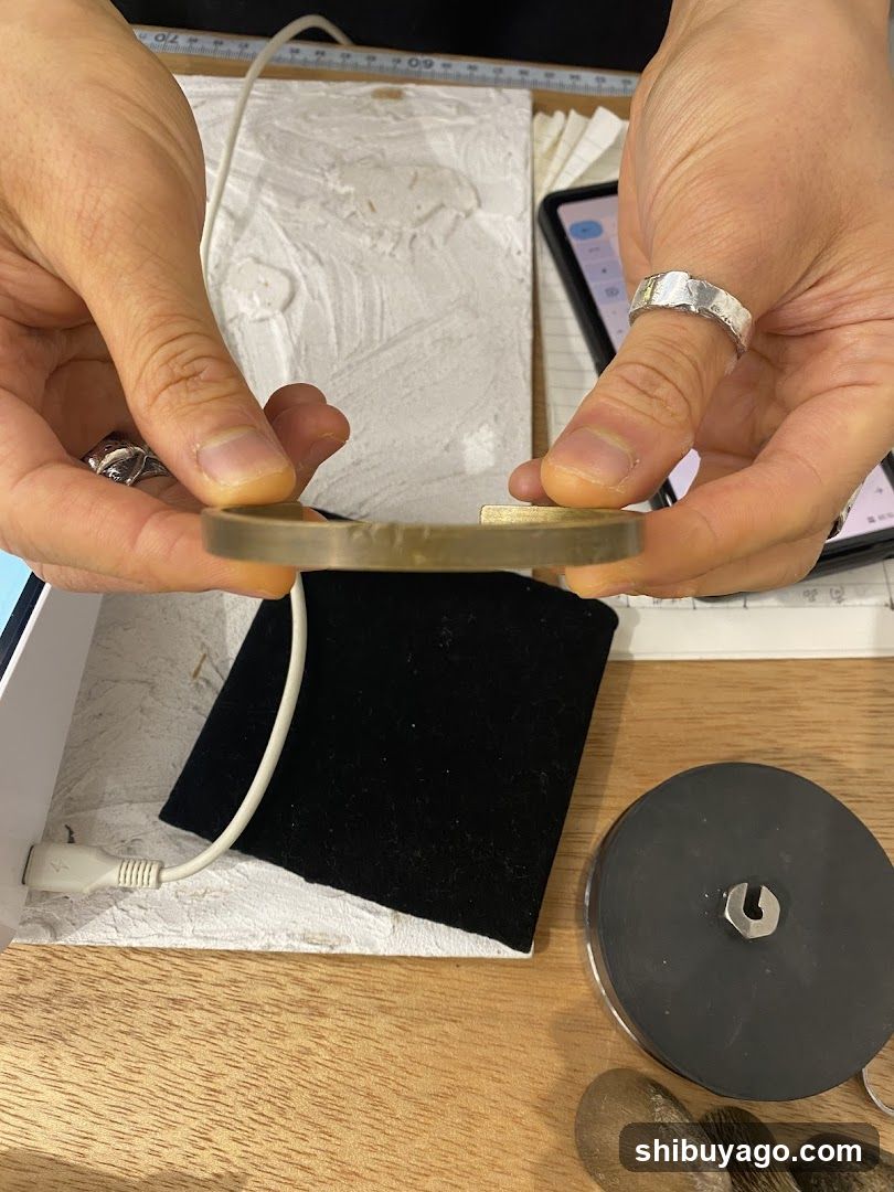 Hands holding a thin metallic ring on a workbench