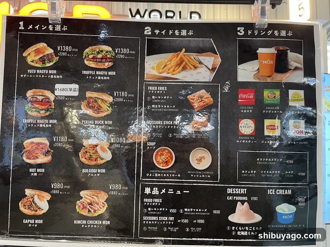 A black menu board with Japanese and English text, featuring three main sections: 'Main', 'Side', and 'Drink'. The menu includes items like Yuzu Wagyu Mor, Truffle Wagyu Mor, Peking Duck Mor, Hot Mor, Bulgogi Mor, Gapad Mor, Kimchi Chicken Mor, Fried Fries, Scissors Stick Fry, Soup options, various sodas (Coca-Cola, Ginger Beer, Lemonade), and desserts like Cat Pudding and Ice Cream.