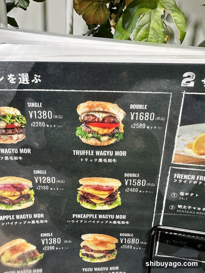 Close-up of a menu board displaying various Wagyu burger options with prices in yen, featuring images and descriptions like Truffle Wagyu Mor, Pineapple Wagyu Mor.